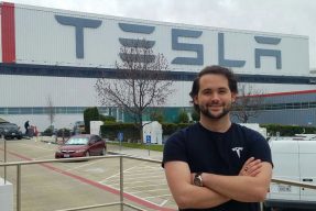 Student poses in front of Tesla facility buildilng