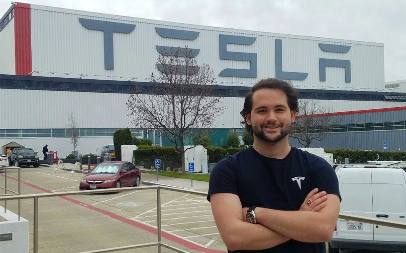 Student poses in front of Tesla facility buildilng