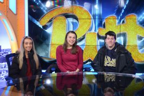 Pitt students behind the desk of the Pitt athletics sports studio space