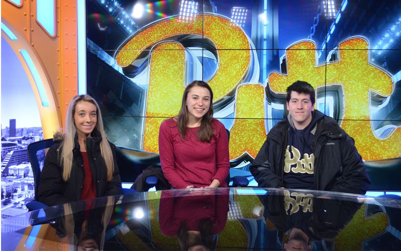 Pitt students behind the desk of the Pitt athletics sports studio space
