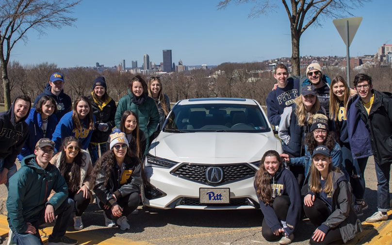 Students pose in front of the Acura car with the City of Pittsburgh in the background
