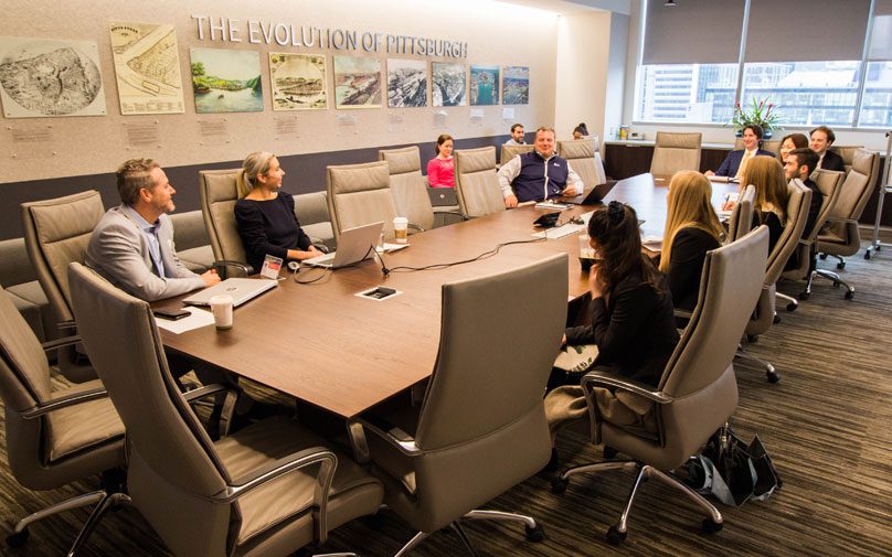Students and employees of JLL gather around the conference room table for a session.