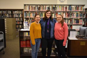 Student tax volunteers pose in front of the library stacks