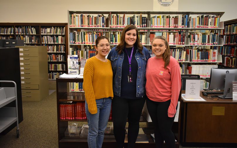 Student tax volunteers pose in front of the library stacks